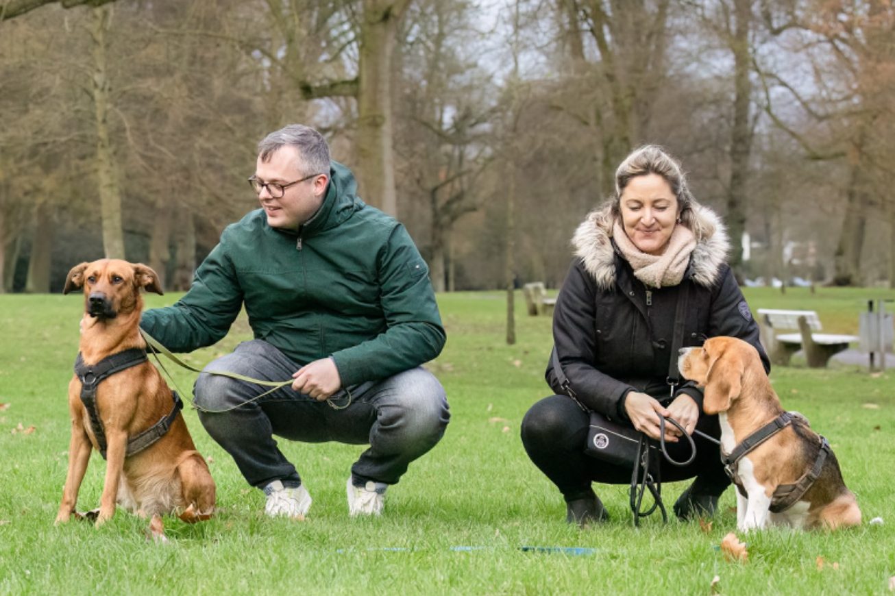 Basis Gruppenkurs: zwei Hundehalter mit ihren Hunden warten auf einem Hundeplatz
