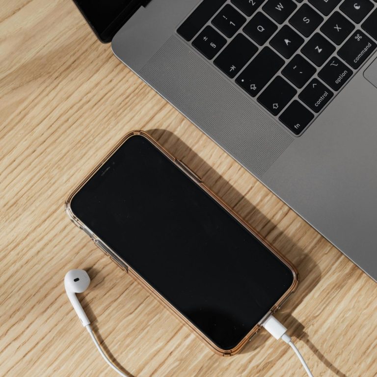 Smartphone mit Kopfhörern liegt neben einem Laptop auf einem Holztisch.